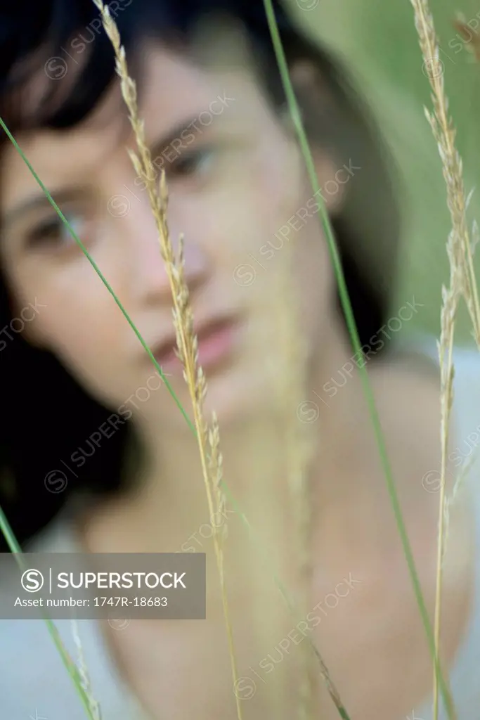 Young woman in tall grass, blurred vegetation in foreground