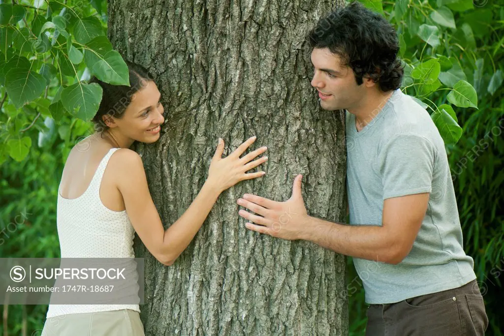 Young couple leaning against tree trunk, smiling at each other