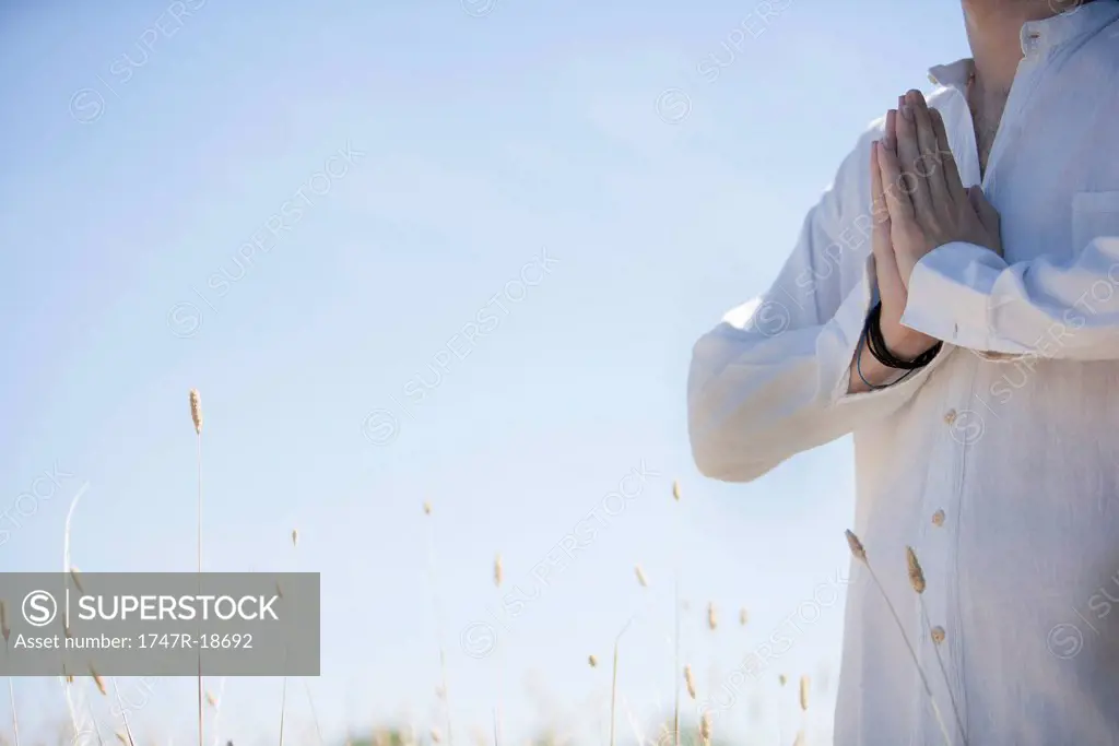 Man outdoors with hands clasped in prayer, cropped