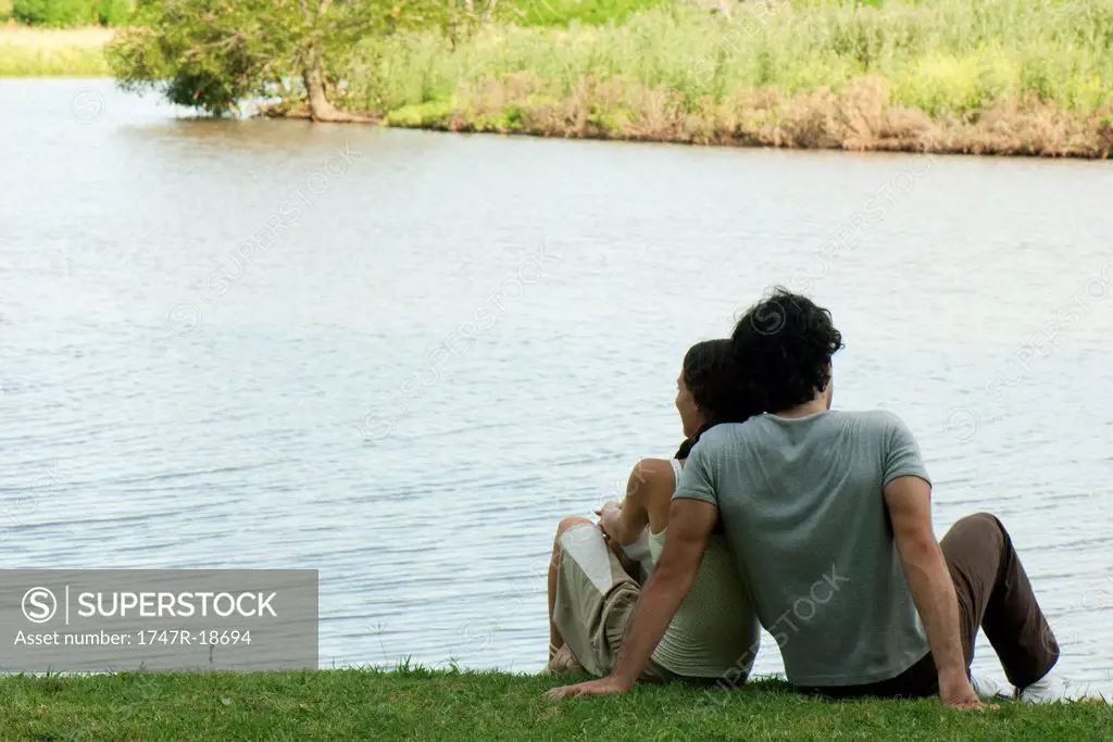 Couple sitting together by lake, rear view