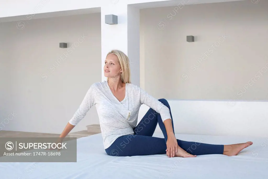 Young woman doing spinal twist yoga pose on bed outdoors