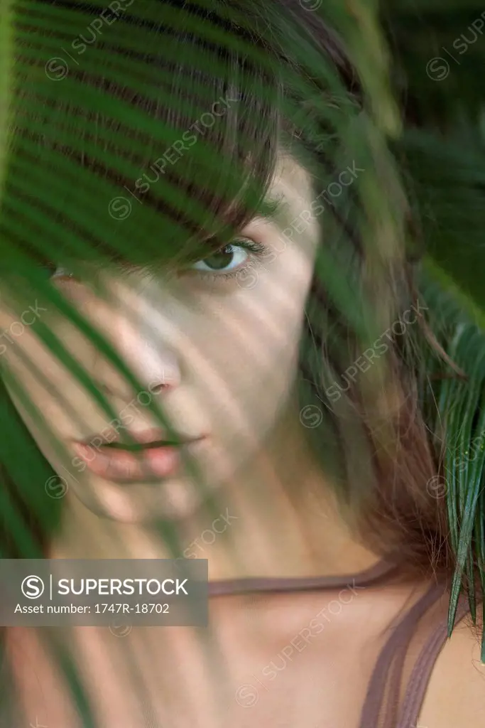 Young woman behind palm frond, portrait