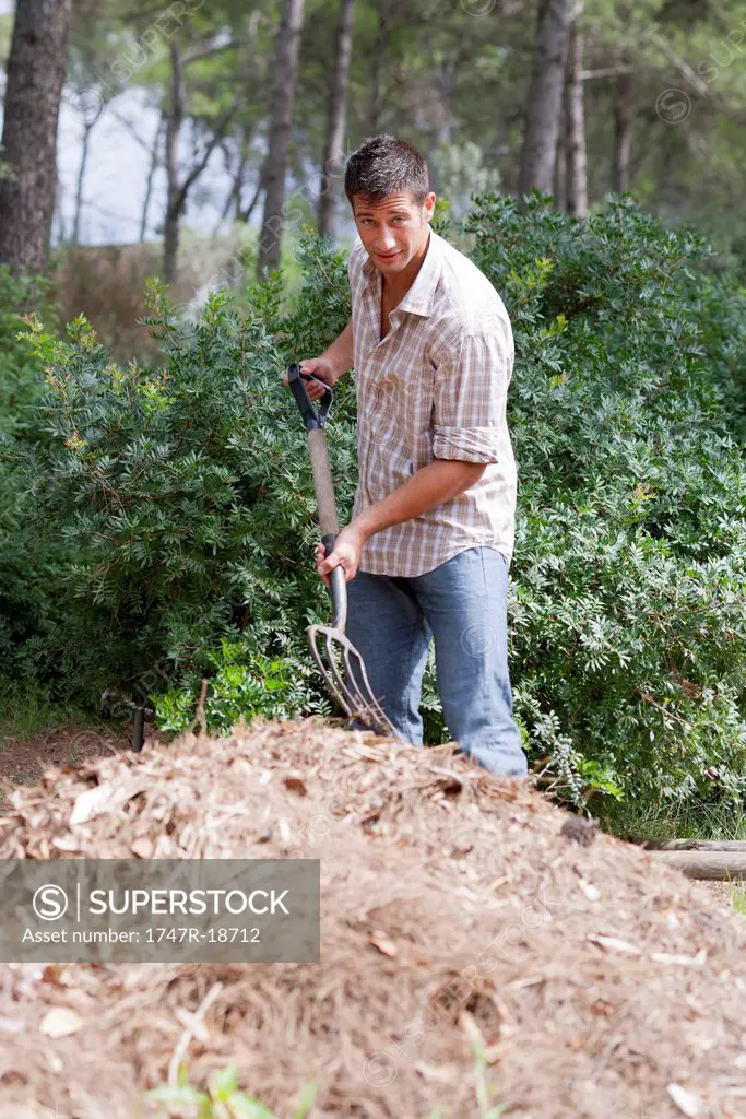 Man standing by heap of straw, holding gardening fork