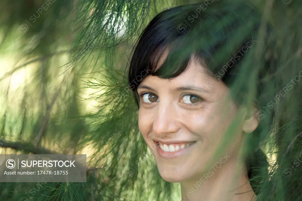 Young woman smiling through pine branches, portrait