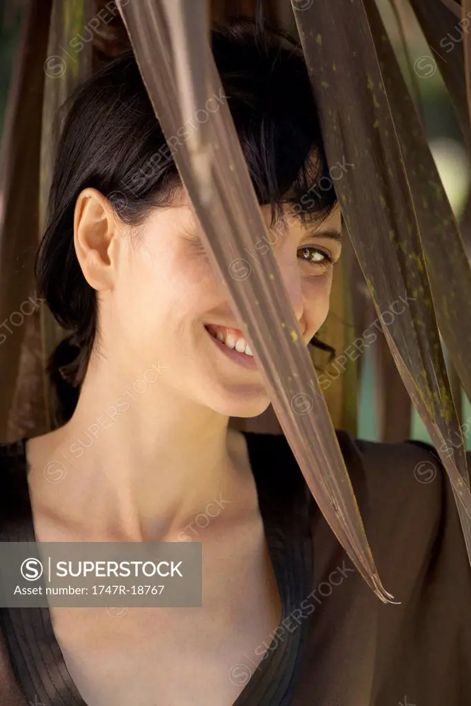 Woman smiling through foliage, portrait