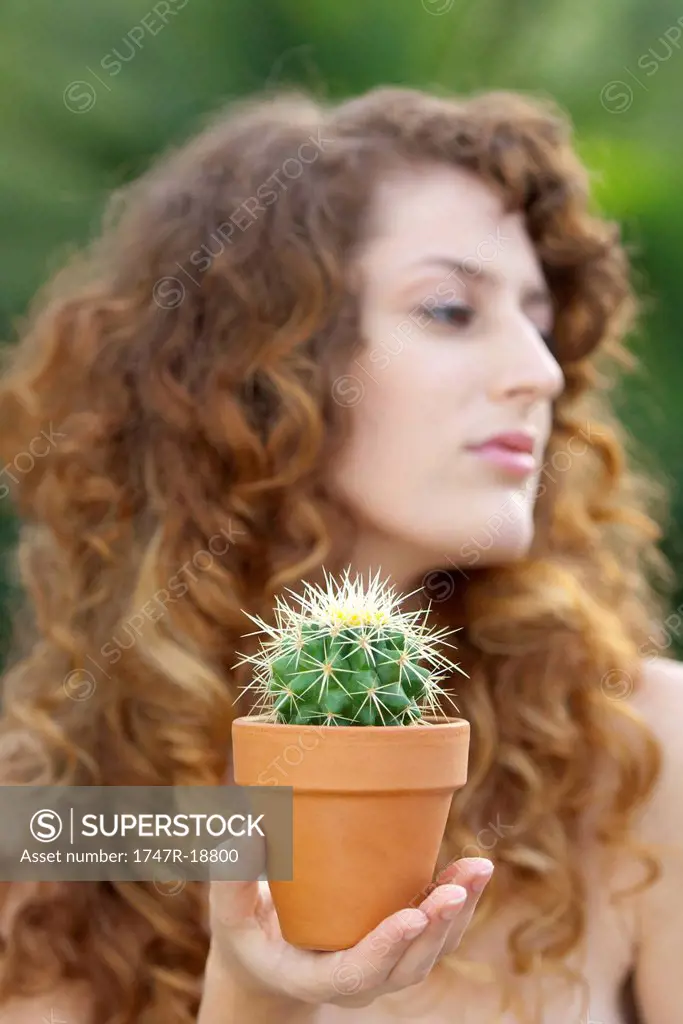 Woman holding potted cactus in palm, looking away