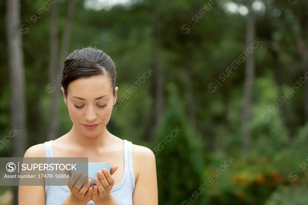 Young woman holding bowl in cupped hands with eyes closed