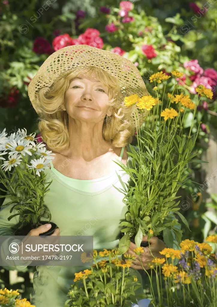 Senior woman holding unpotted flowers, looking at camera