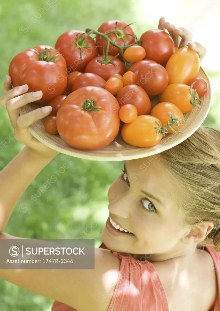 Woman holding bowl full of tomatoes on top of head