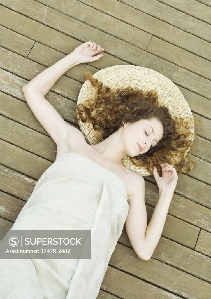 Woman lying on deck, wrapped in towel, head on mat