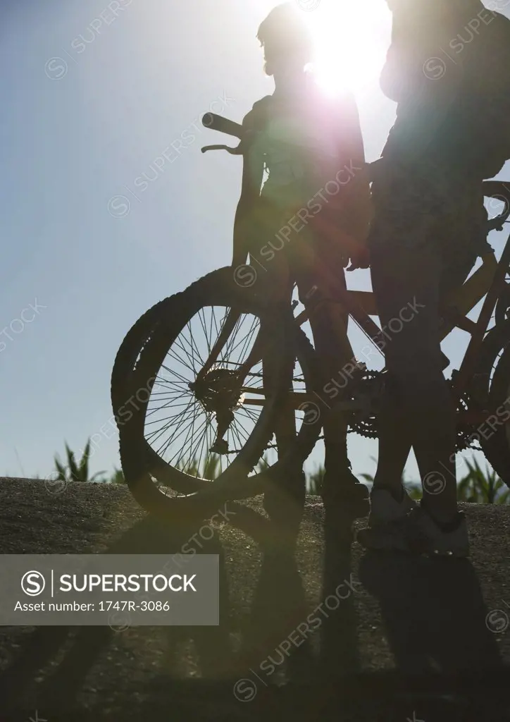 Mountain bikers standing by bikes, backlit