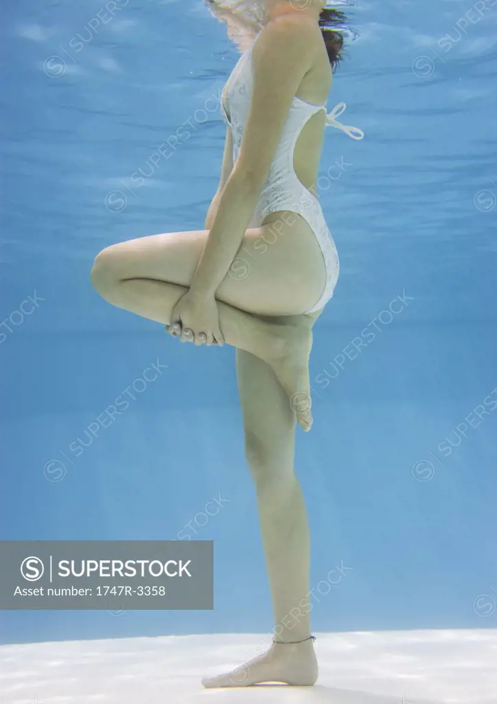 Teenage girl holding knee in pool, underwater view