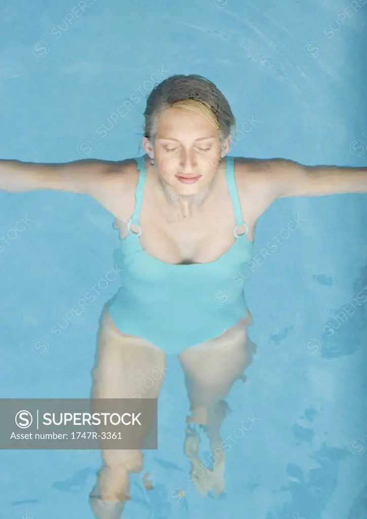 Young woman floating on back in pool, eyes shut