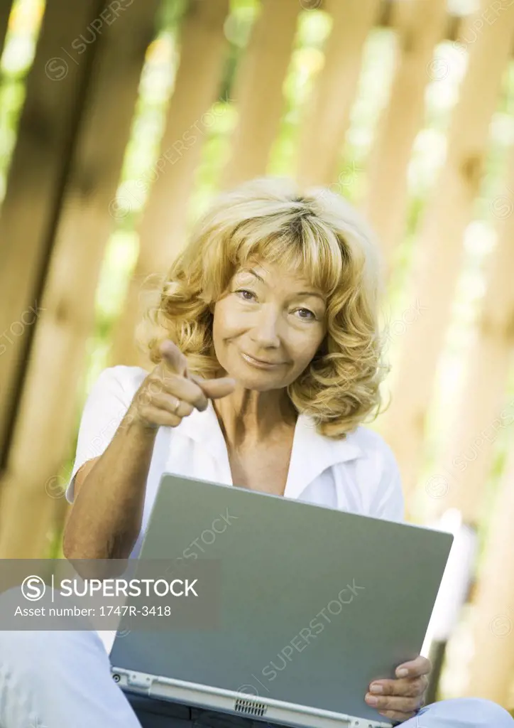 Senior woman using laptop, pointing at camera