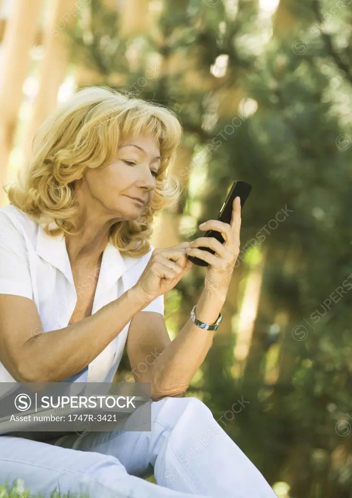 Senior woman using cell phone, laptop on lap, outdoors