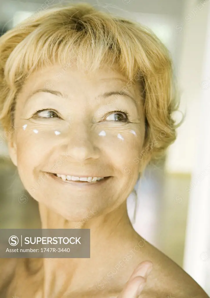 Senior woman with dollops of moisturizer under eyes