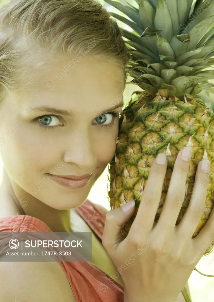 Woman holding pineapple next to face, smiling at camera