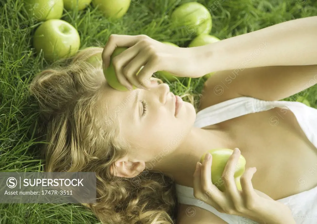 Woman lying in grass, holding apple to forehead