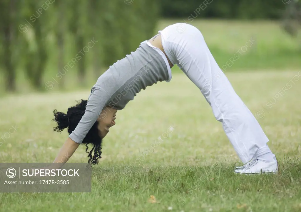 Young woman doing downward dog pose on grass