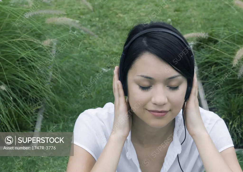 Woman sitting in ornamental garden, listening to headphones