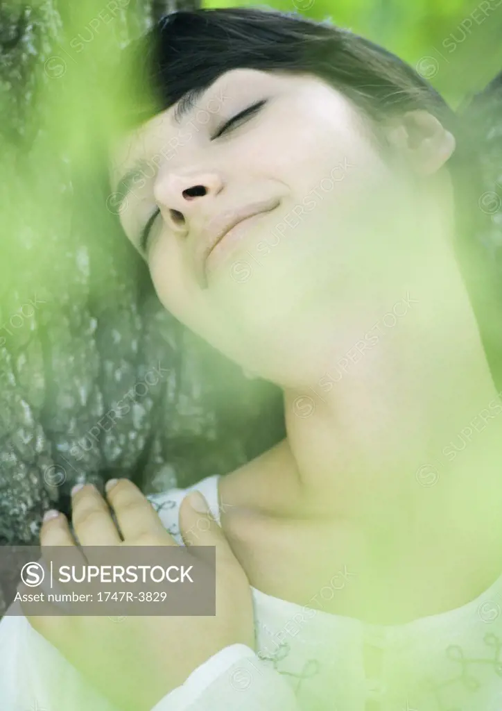Woman leaning against tree, eyes closed