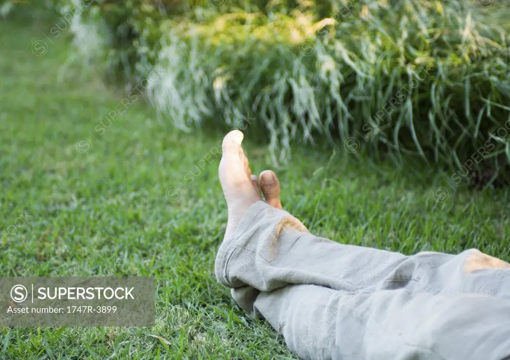 Man's legs on grass, barefoot, knee down