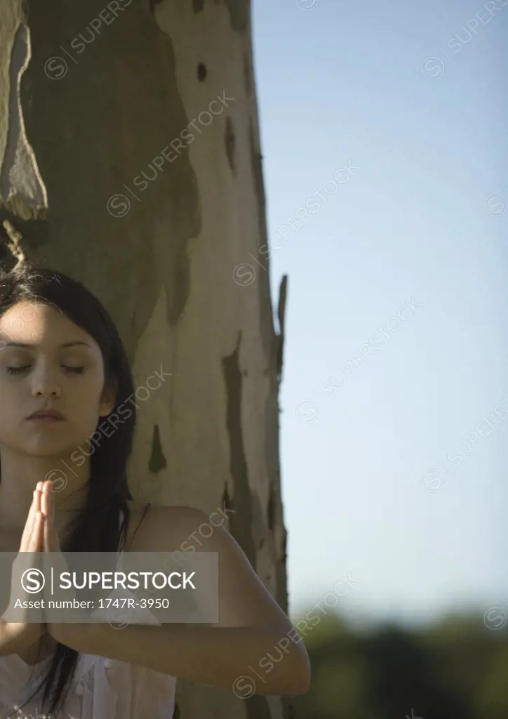 Woman standing in prayer position near tree