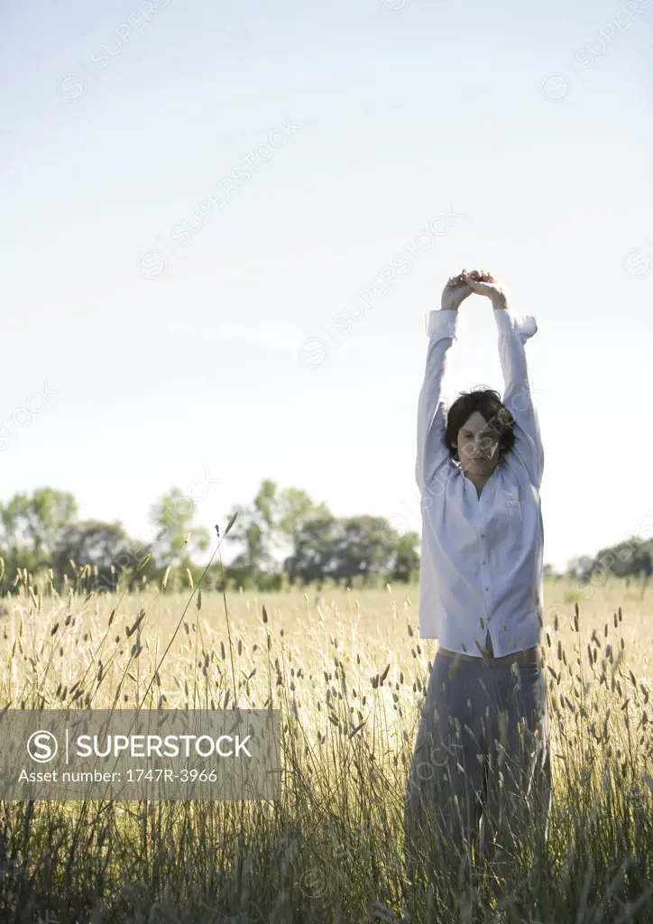 Man standing stretching arms over head in field