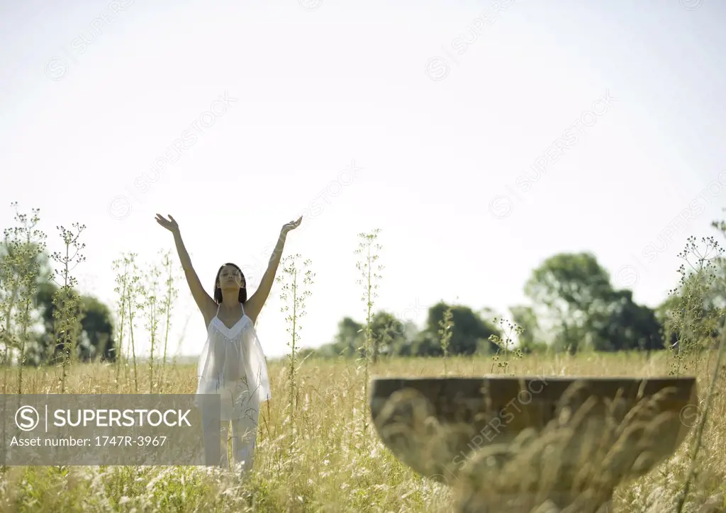 Woman standing in sun salutation pose, in field