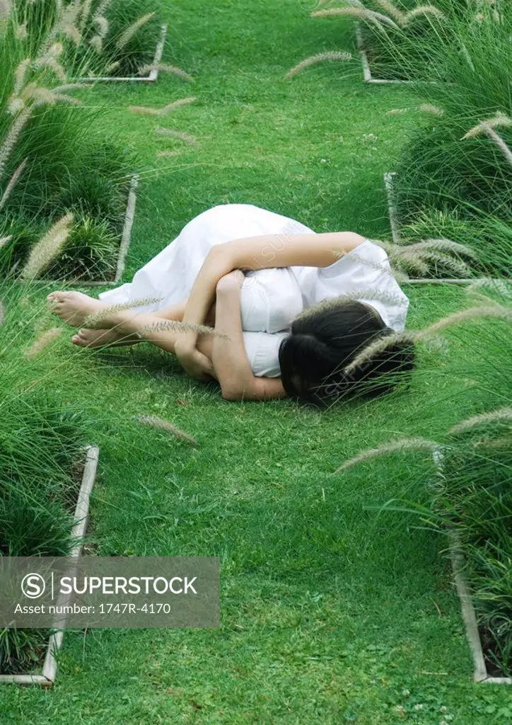 Woman curled up in fetal position on grass