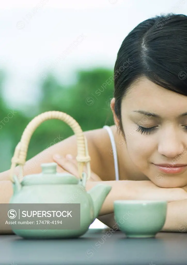 Woman resting head on arms near tea service