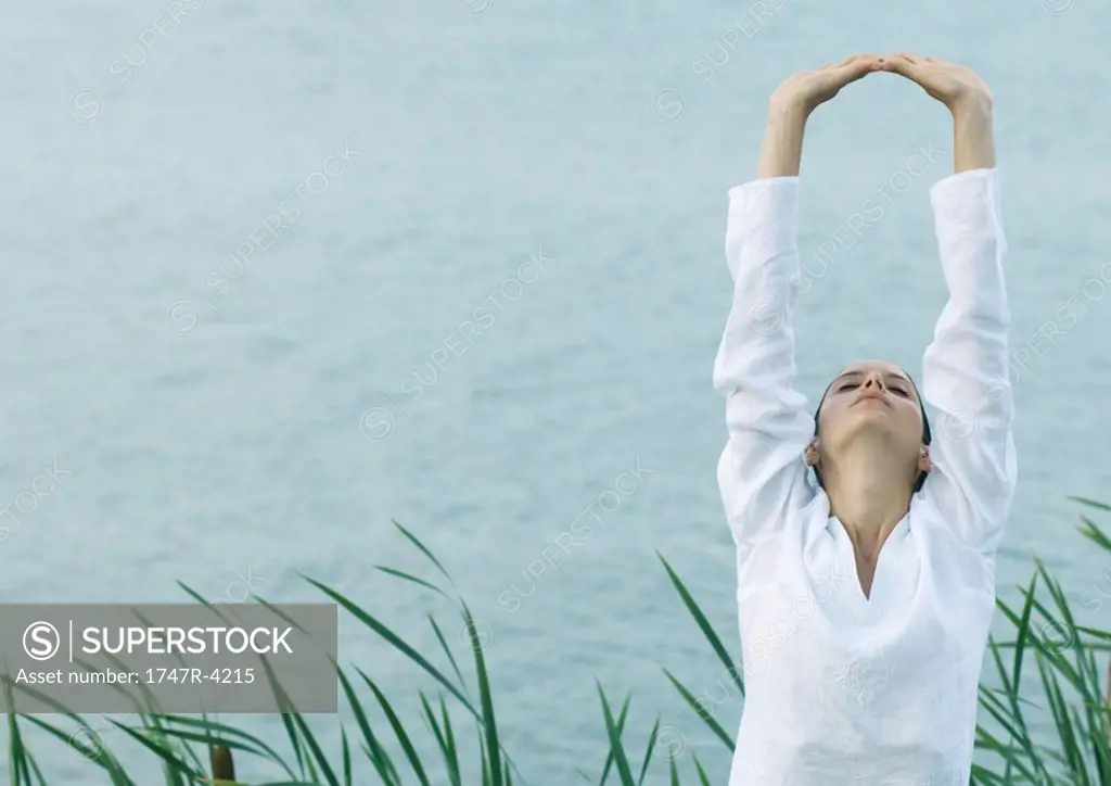 Woman stretching arms over head, lake in background