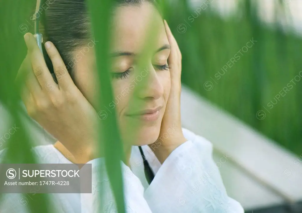 Woman listening to headphones, eyes closed, hands over ears