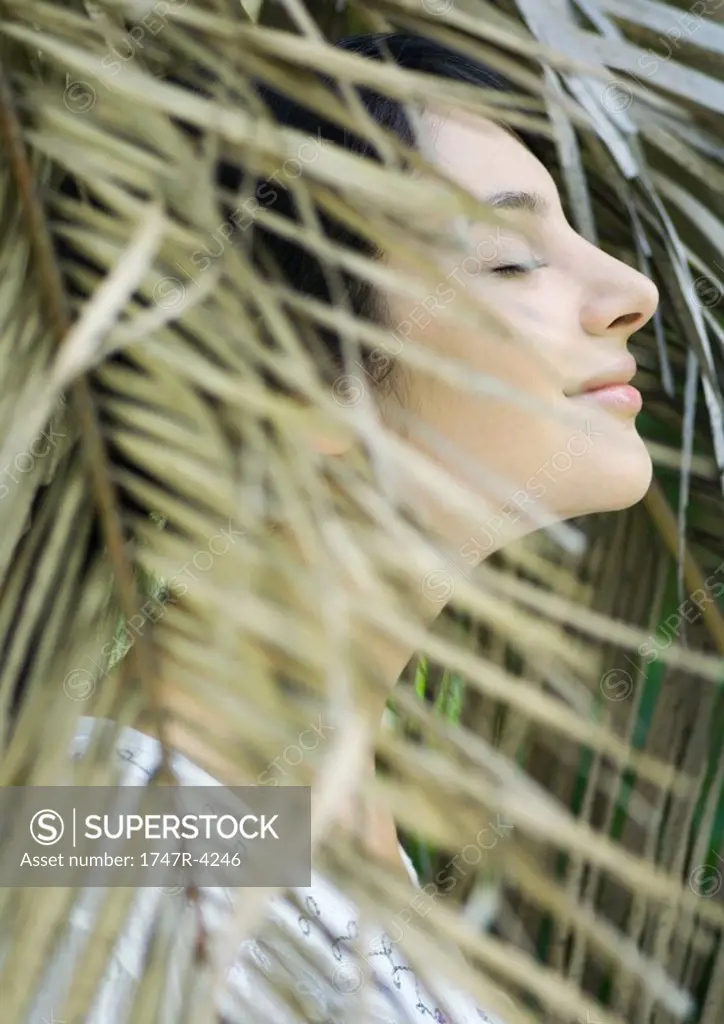 Woman standing in foliage, eyes closed, side view