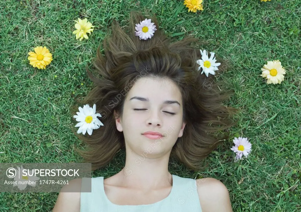 Woman lying on grass with flowers scattered around head, eyes closed