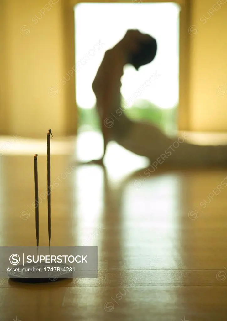 Woman doing cobra pose, side view, focus on incense in foreground
