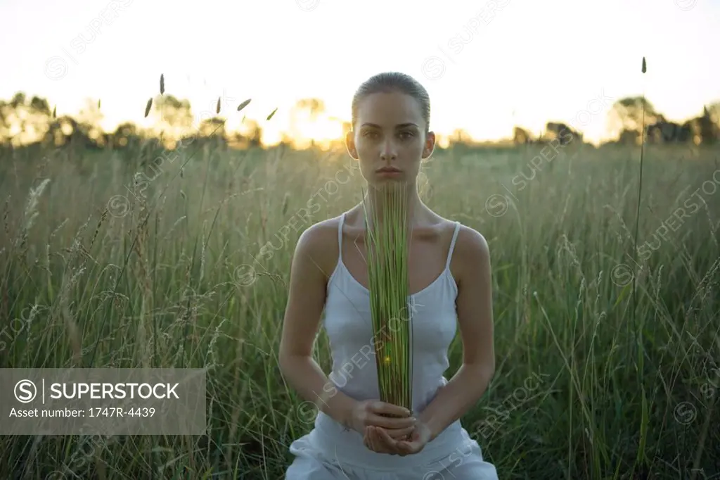 Woman sitting in field, holding rushes in hands
