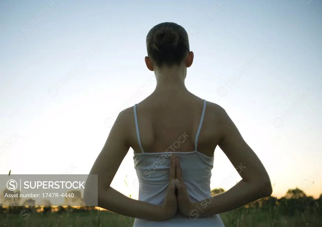 Woman doing yoga pose, hands clasped behind back, at sunset