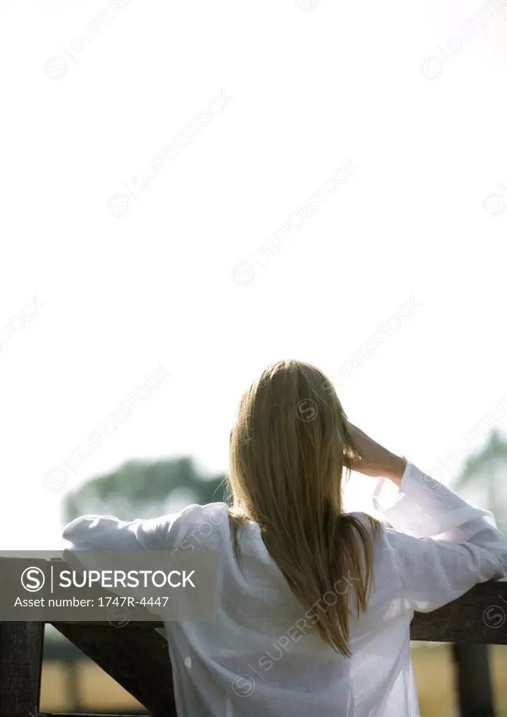 Woman leaning against wooden fence, rear view