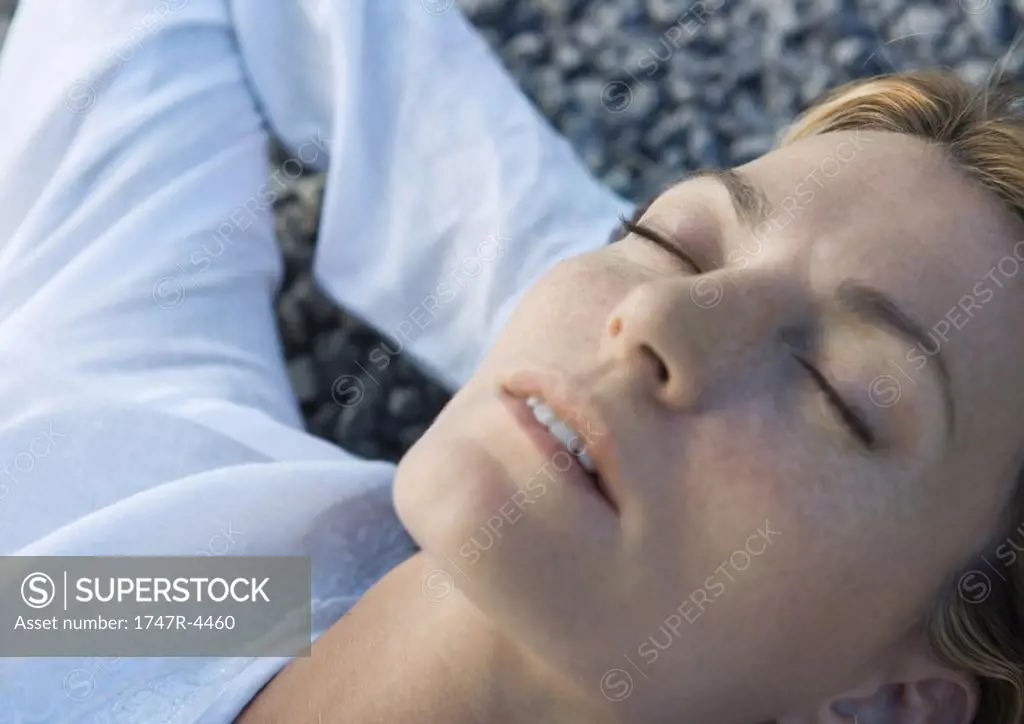 Woman lying on gravel with hands behind head, eyes closed, close-up