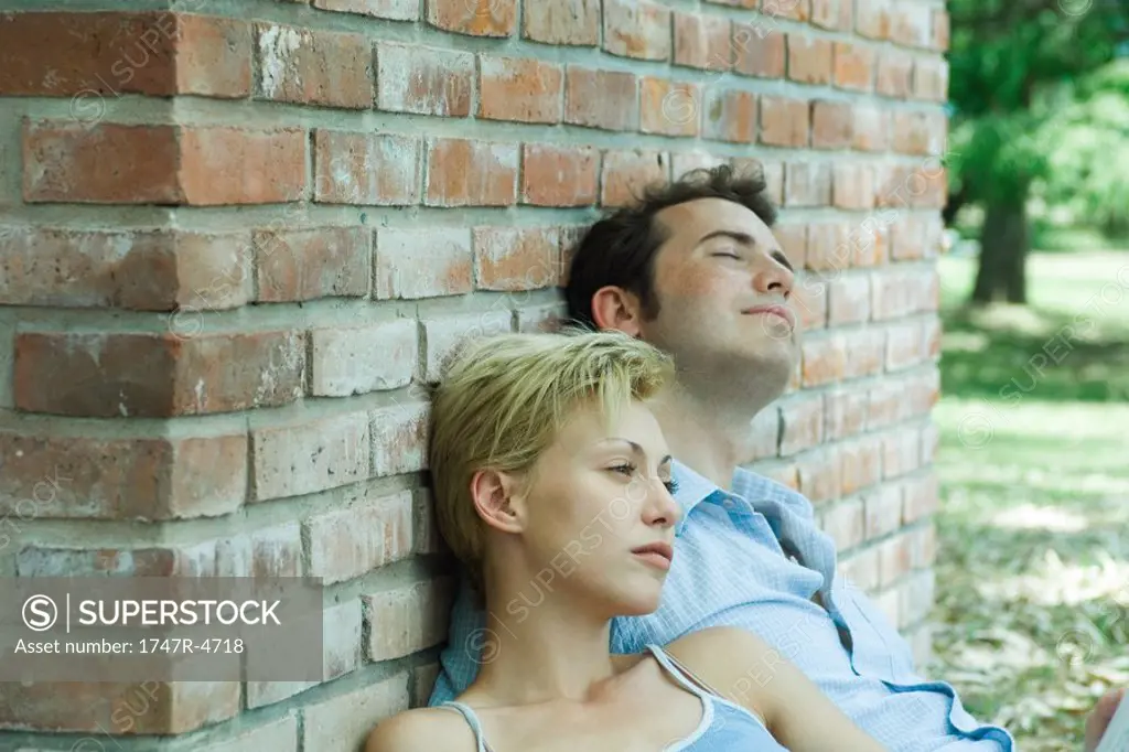 Couple sitting outdoors, leaning against brick wall