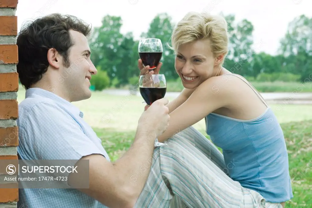Couple sitting outdoors, toasting with glasses of red wine