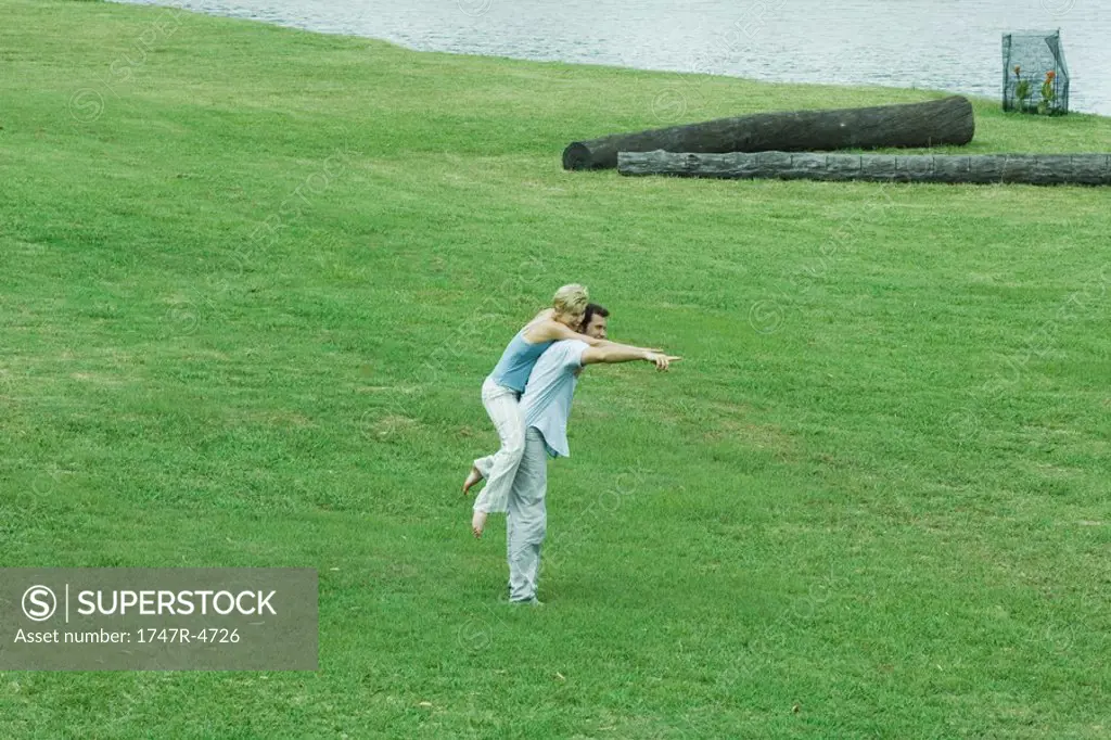 Couple on lawn, man holding woman piggyback, pointing to distance