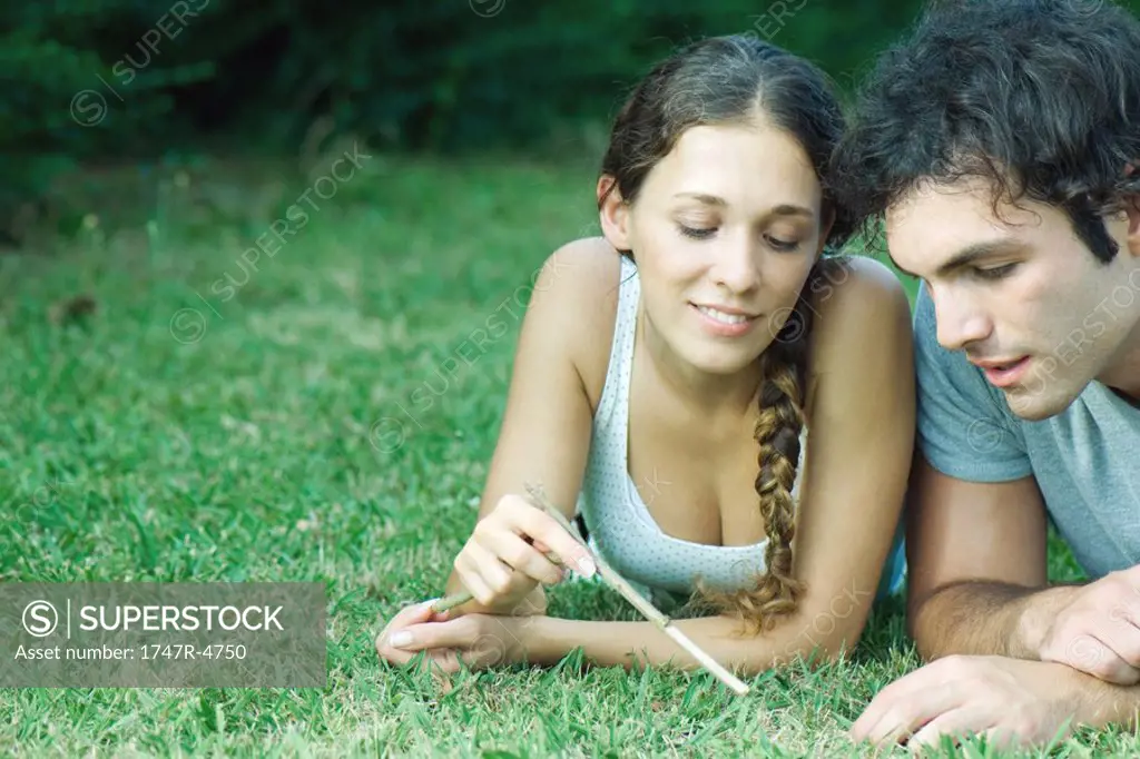 Couple lying in grass, woman holding twig