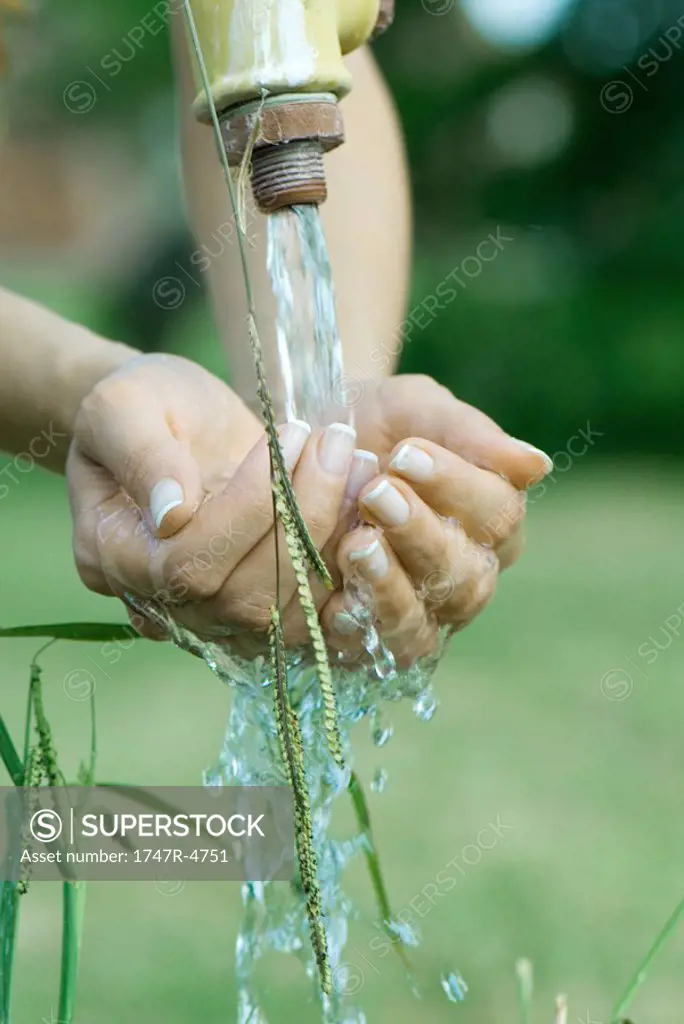 Woman cupping hands under outdoor faucet, close-up, cropped view of hands