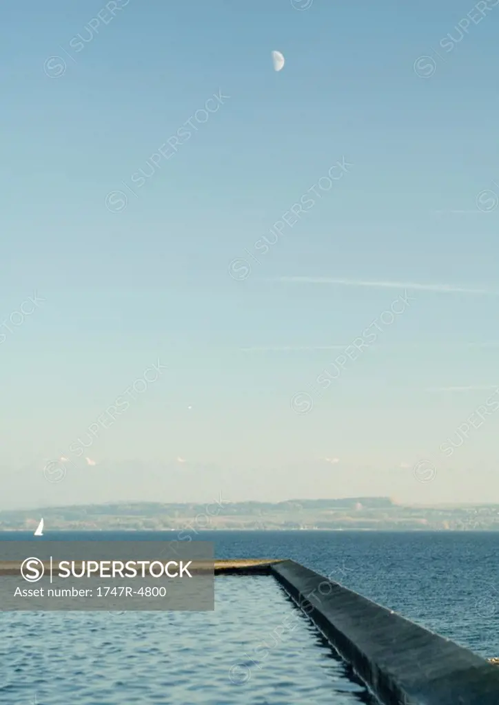 Seascape with breakwater in foreground and sailboat in distance