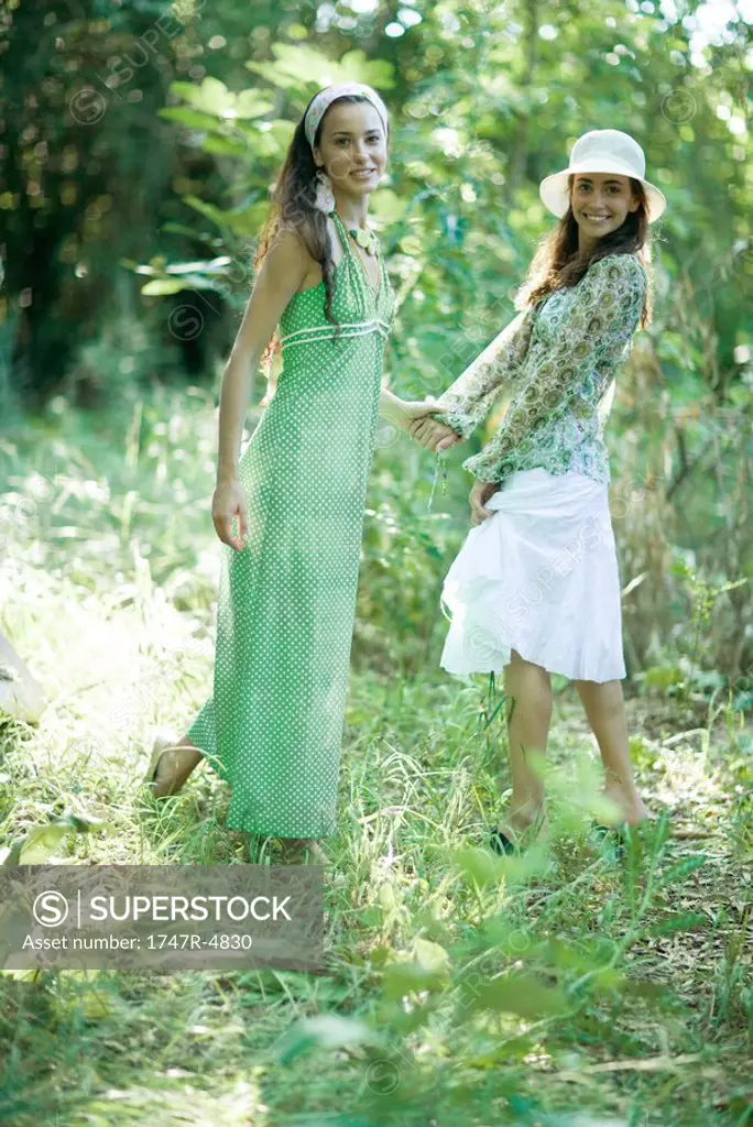 Two young women standing in woods, holding hands