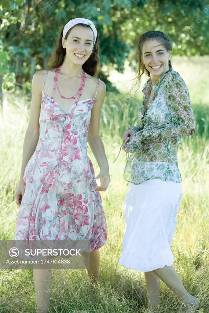 Two young women standing in field, smiling at camera