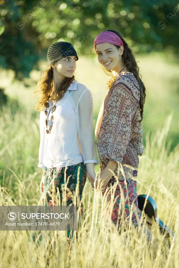 Young hippie women standing in field, one holding guitar and smiling at camera