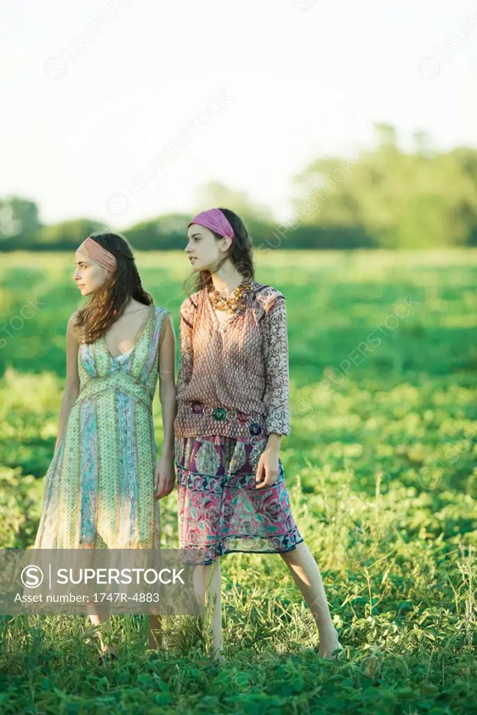 Young hippie women standing in field, looking away, full length